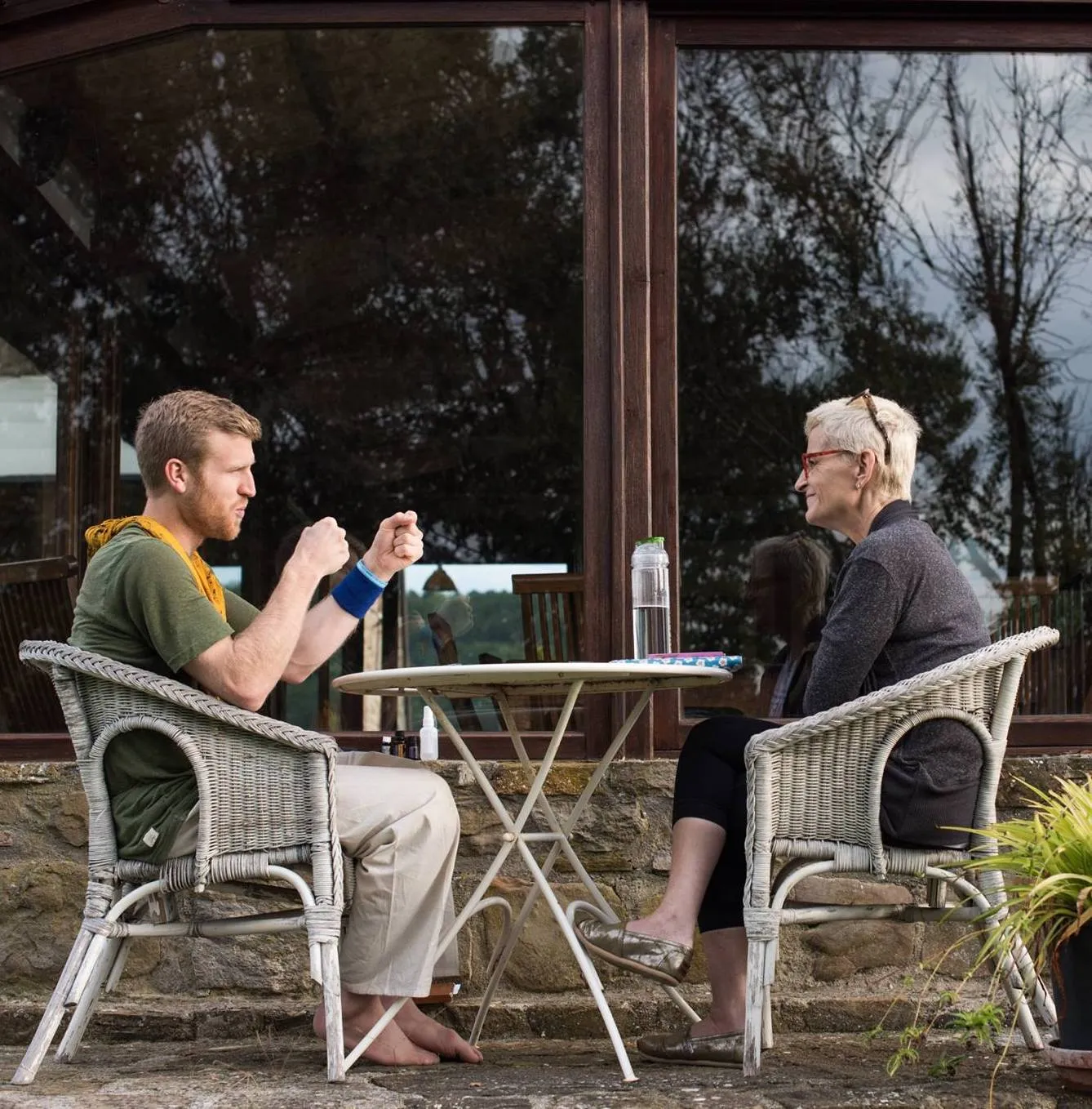 Telfer and a client in wicker chairs at a small table on a stone terrace, deep in conversation.