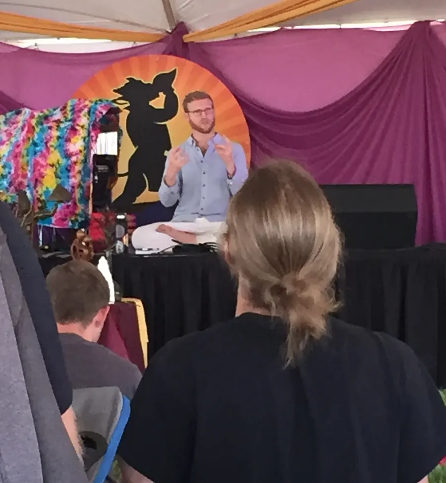 Telfer seated cross-legged on a festival stage under a tent, speaking to a seated audience.