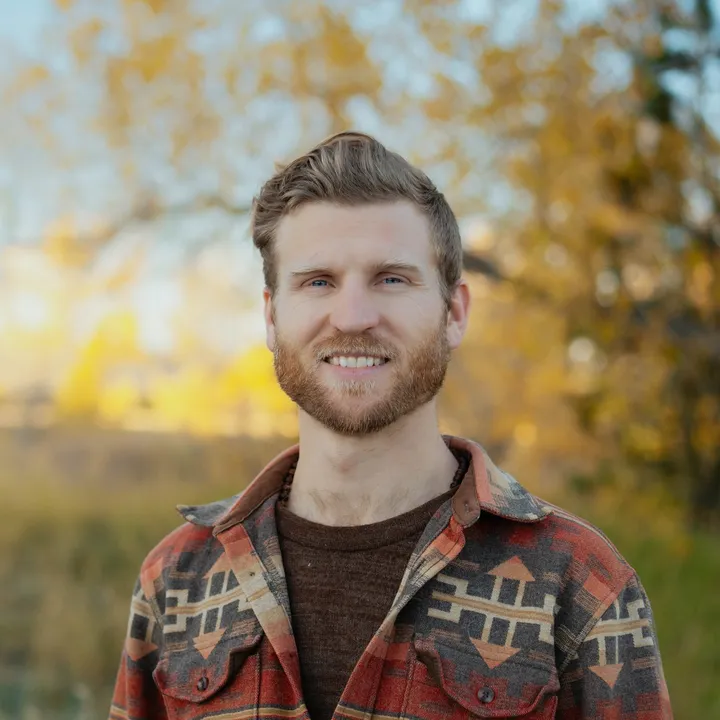Telfer standing in a golden autumn field in a red patterned flannel jacket.