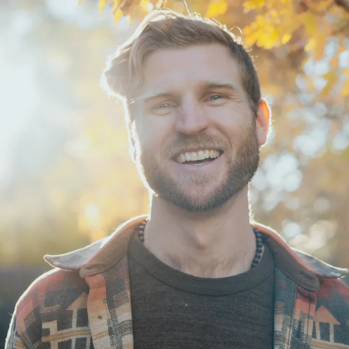 Telfer smiling in warm autumn sunlight, wearing a red patterned flannel jacket.