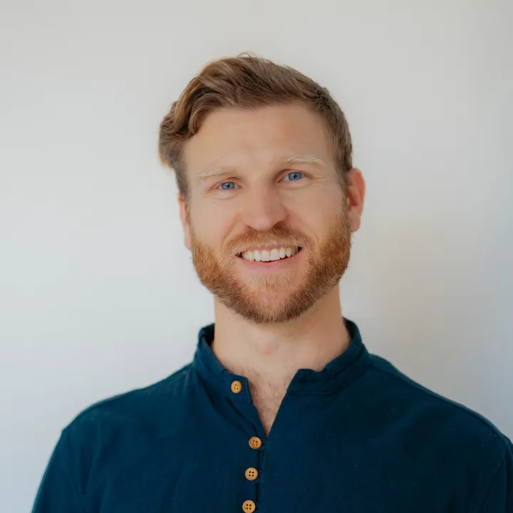 Telfer smiling against a plain white wall, wearing a dark blue henley.