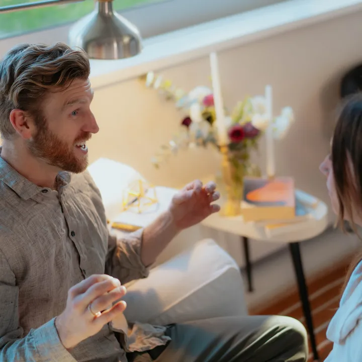 Telfer in a linen shirt talking with someone in a bright, plant-filled room.